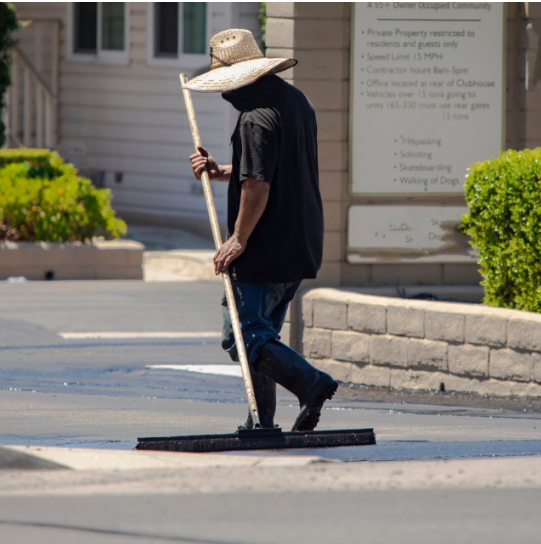 A professional worker using a specialized broom-like tool to evenly smooth the surface during an asphalt sealcoating project, demonstrating the expertise of A-Top Paving, DBA of Florida Paving Pros, in providing high-quality sealcoating services in Palm Beach County.