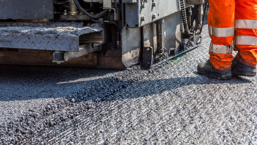 Close-up view of an asphalt milling machine in action, with a worker in safety gear standing nearby, illustrating the expertise of A-Top Paving, DBA of Florida Paving Pros, in providing professional asphalt milling services in Palm Beach County.